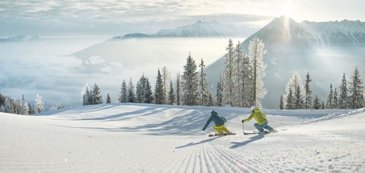 two skiiers skiiing down mountain ski slope with clouds in background